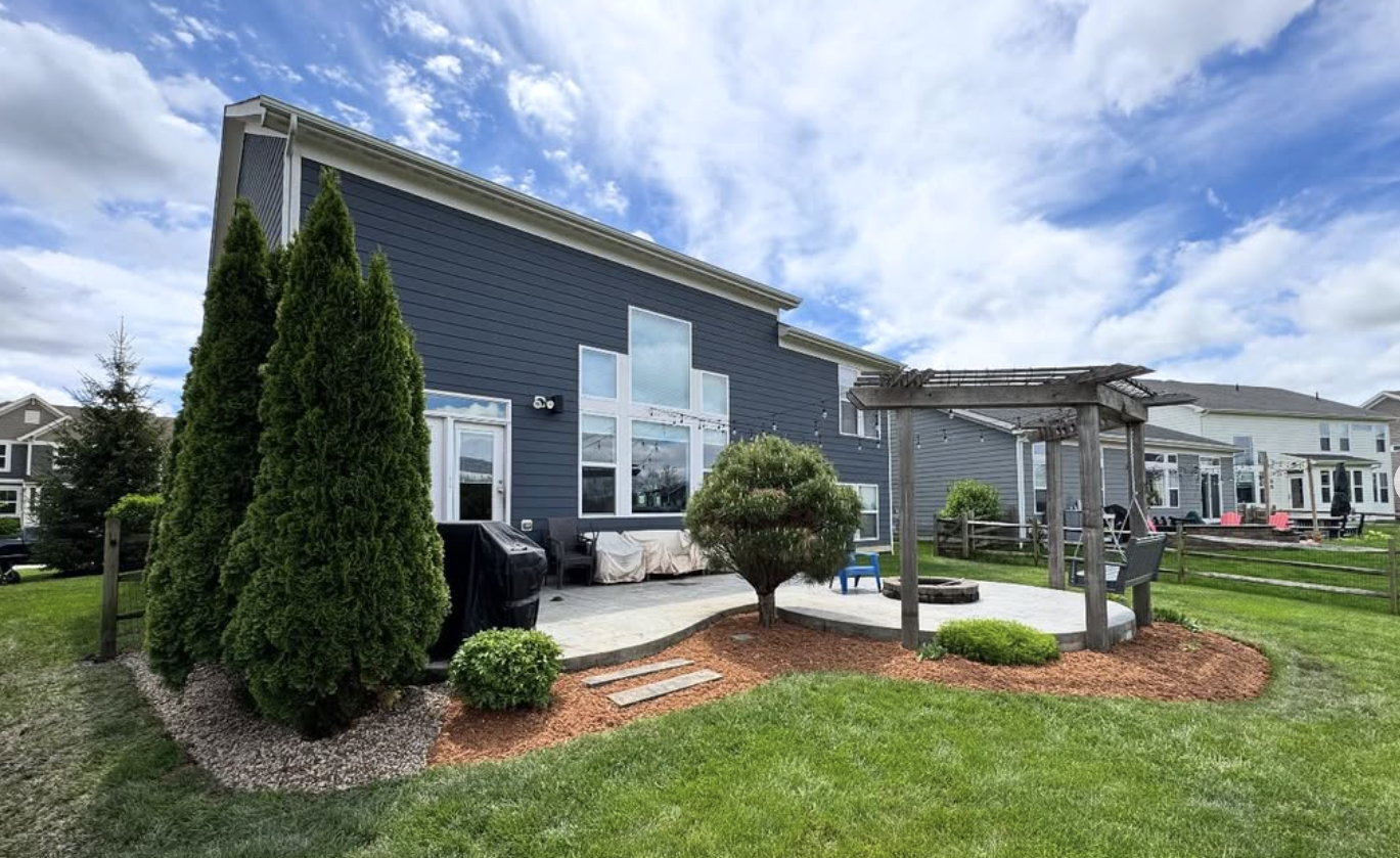 Modern home with sculpted boxwoods, mulched bedlines, and a pergola — clean installation work